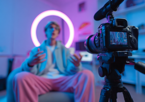 Un créateur de contenu en train d’enregistrer une vidéo face à une caméra, entouré d’un éclairage néon circulaire en arrière-plan dans une ambiance studio.