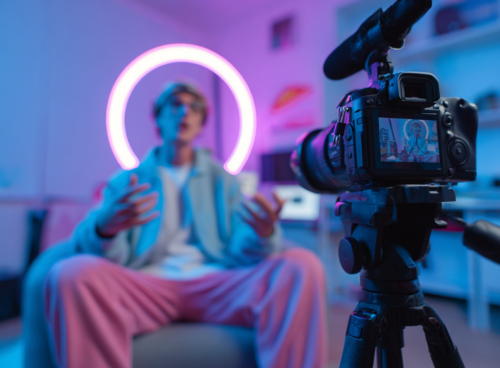 Un créateur de contenu en train d’enregistrer une vidéo face à une caméra, entouré d’un éclairage néon circulaire en arrière-plan dans une ambiance studio.